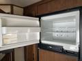 An open refrigerator with a white interior displaying empty shelves and a removable storage bin in a 2016 Jayco 265RLSW