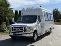 A white 2013 Ford Econoline van with multiple windows and a raised roof, featuring chrome accents and front grille, parked on a street