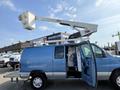 A blue 2010 Ford Econoline van with its side door open and an elevated bucket lift attached on top