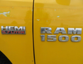 Close-up of the badges on a yellow 2015 RAM 1500 displaying HEMI 5.7 LITER and RAM 1500 in chrome lettering