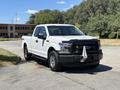 A white 2016 Ford F-150 pickup truck with a black grille and chrome wheels facing the camera with a noticeable hood ornament