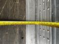 A measuring tape lies flat on a surface, displaying various measurement markings in centimeters and inches, with a portion extending towards a metal edge