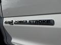 A close-up of a chrome badge on a white truck displaying the text 6.7L POWER STROKE TURBO DIESEL
