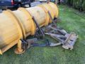 A yellow snow plow attachment for a truck with a curved blade and spring-mounted pivot arms resting on grass