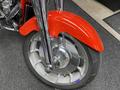 A close-up view of the front wheel and fender of a 2024 Harley Davidson Fat Boy showing chrome accents and a red fender