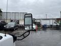 A 2020 Chevrolet Express van is parked in a lot with raindrops on the mirror reflecting other vehicles and a fence