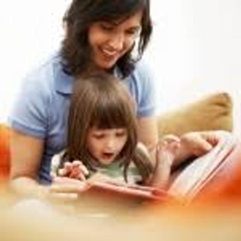A caregiver and a young girl sit together reading a book with excitement and engagement