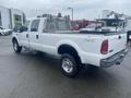 A white 2005 Ford F-350 Super Duty pickup truck with a crew cab and a flatbed, featuring chrome wheels and a mesh tool compartment on the truck bed