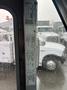 A 2012 Ford Econoline bus with a white exterior is partially visible through a rain-splattered window showing specifications and information on the window frame