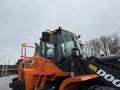 A 2018 Doosan DL300-5 wheel loader featuring an orange and black exterior and a large bucket attached at the front
