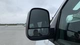 A side mirror of a 2017 Chevrolet Express Quigley 4x4 displaying a reflection of a person