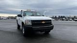 A white 2013 Chevrolet Silverado 1500 pickup truck with a yellow light bar on the roof parked in an empty lot