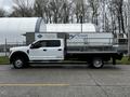 A white 2017 Ford F-550 flatbed truck parked on the street with a metal frame and a flat cargo area