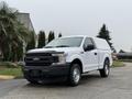 A white 2018 Ford F-150 with a black grille and truck bed cap is parked on a driveway