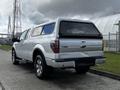 A silver 2014 Ford F-150 with a truck cap on the bed parked on a street with a visible trailer hitch and chrome wheels