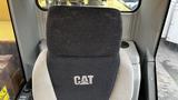 A close-up of the operator's seat in a 2018 Caterpillar 326F L Excavator featuring a black and gray design with the CAT logo prominently displayed