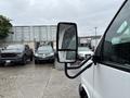A 2020 Chevrolet Express van with a side mirror reflecting another vehicle and raindrops on the mirror surface