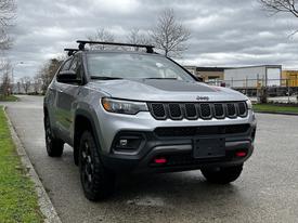 A 2023 Jeep Compass in silver with a roof rack and blacked-out wheels parked on a street