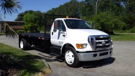 White 2006 Ford F-650 flatbed truck with a black flatbed and orange side mirrors parked on a street