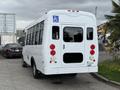 A white 2013 Chevrolet Express shuttle bus with a wheelchair access symbol on the side and red taillights is parked, showing the rear view