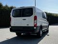 A white 2023 Ford Transit van viewed from the rear with large windows and a high roof