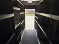 Interior view of a 2016 Ford Transit with metal shelving on both sides and an empty aisle leading to the rear doors