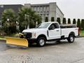 A white 2023 Ford F-250 pickup truck equipped with a yellow snow plow attached to the front
