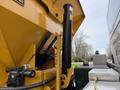 A close-up view of the hydraulic mechanism of a yellow industrial truck showing the raised dump bed and attached components