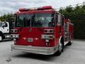 A red 1991 Sutphen Deluge fire truck with a polished front bumper multiple lights on top and a shiny chrome grille featuring emblems and a large windshield