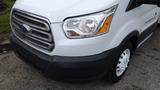 A white 2018 Ford Transit van with a silver grille and round headlights visible in the foreground and a black bumper below