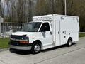A white 2013 Chevrolet Express with a boxy cargo area and emergency lights on top parked on a concrete surface