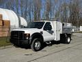 A 2008 Ford F-450 SD with a white exterior features a flatbed and storage compartments on the side