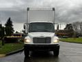 A 2018 Freightliner M2 106 box truck is shown head-on with its lights illuminated and a white cargo area in the background