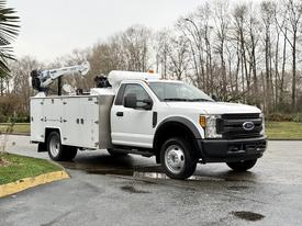 A white 2017 Ford F-550 bucket truck with a mounted lift and utility storage compartments on the side