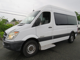 A white 2009 Dodge Sprinter Van with a gray lower body and large windows parked on the side of the road