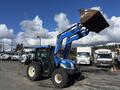 A blue and black 2010 New Holland T4050 tractor with a raised front loader bucket and large tires