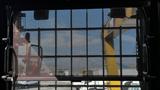 A 2018 Caterpillar 326F L Excavator visible through a mesh protective screen with controls and a visible yellow arm extending into the view