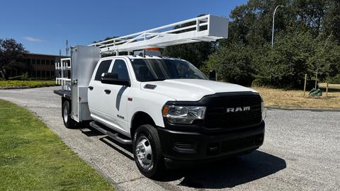 A white 2019 RAM 3500 truck with a flatbed and a ladder rack mounted on top parked on a road