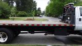 A 2008 Ford F-750 flatbed truck with a wooden bed and black undercarriage displayed on a street