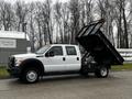 A 2015 Ford F-550 with a dump truck bed raised, featuring a white exterior and multiple axles, parked with the driver's side facing the viewer