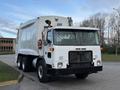 A 2010 Autocar Xpeditor garbage truck with a white exterior and a front cab featuring multiple lights and a grille on the front with side mirrors and large wheels