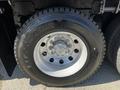 A close-up view of the tire and wheel of a 2012 Freightliner M2 112 featuring a silver alloy rim and a black Firestone tire with prominent tread patterns