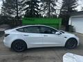 A 2022 Tesla Model 3 in white with black wheels parked on a driveway