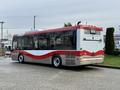 A 2016 Grande West Vicinity bus with a red and white design parked at a facility showing its side and rear features