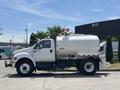 A white 2015 Ford F-750 water truck with a rounded water tank and side-mounted pump system