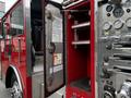 A red 1991 Sutphen Deluge fire truck with an open compartment door revealing shelves and control panels including gauges and knobs