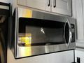A stainless steel microwave with a black glass door and a digital control panel is mounted above kitchen cabinets