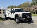 A white 2015 Ford F-550 pickup truck with a utility bed and emergency beacon lights on top parked on a street