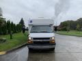 A white 2015 Chevrolet Express with a large front windshield and a blue wheelchair accessibility symbol on the side facing forward