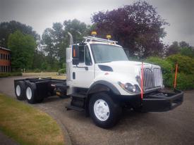 A white 2012 International 7400 truck with a raised hood and orange safety lights on top parked with no cargo in the truck bed